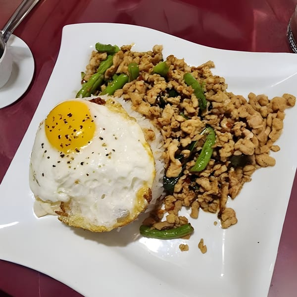 Thai basil chicken with rice and a fried egg, garnished with black pepper, on a white plate.