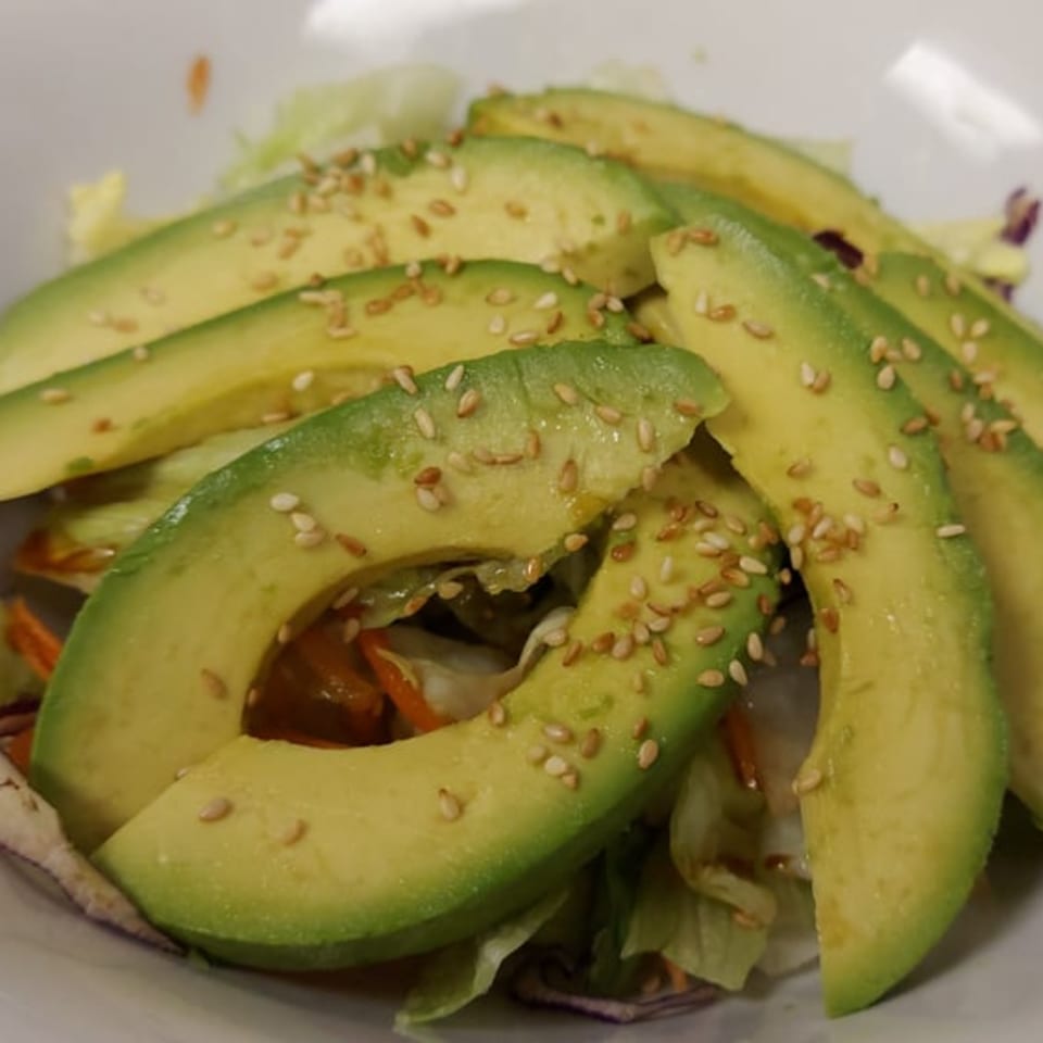Close-up of a Thai avocado salad with sesame seeds, lettuce, and carrots.