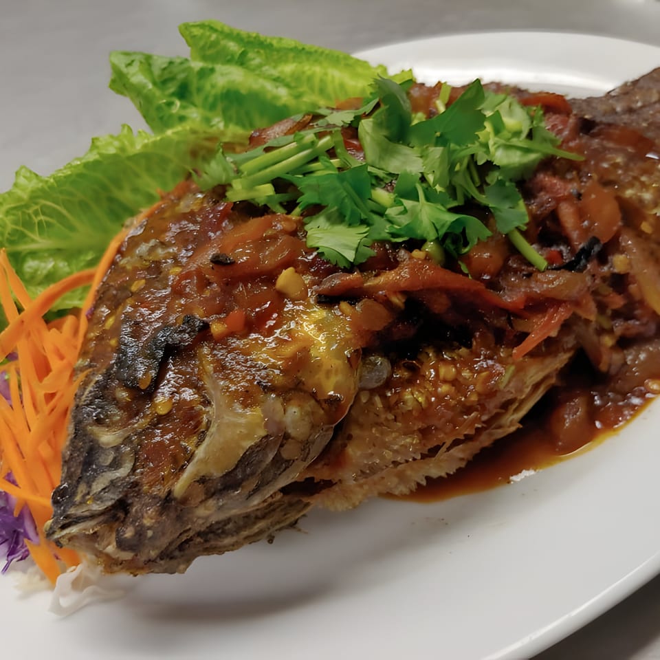 Whole fried fish covered in a rich brown sauce, topped with cilantro and served with lettuce and carrots.